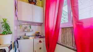 Una cocina compacta con armarios blancos, un lavabo y un ventanal con cortinas rojas.