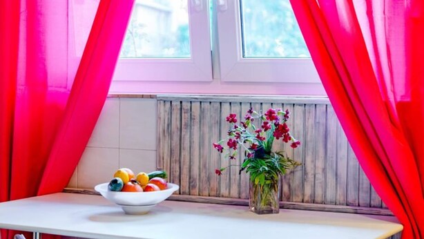 Una cocina con un tazón de fruta en la encimera, un florero con flores y una ventana con cortinas.