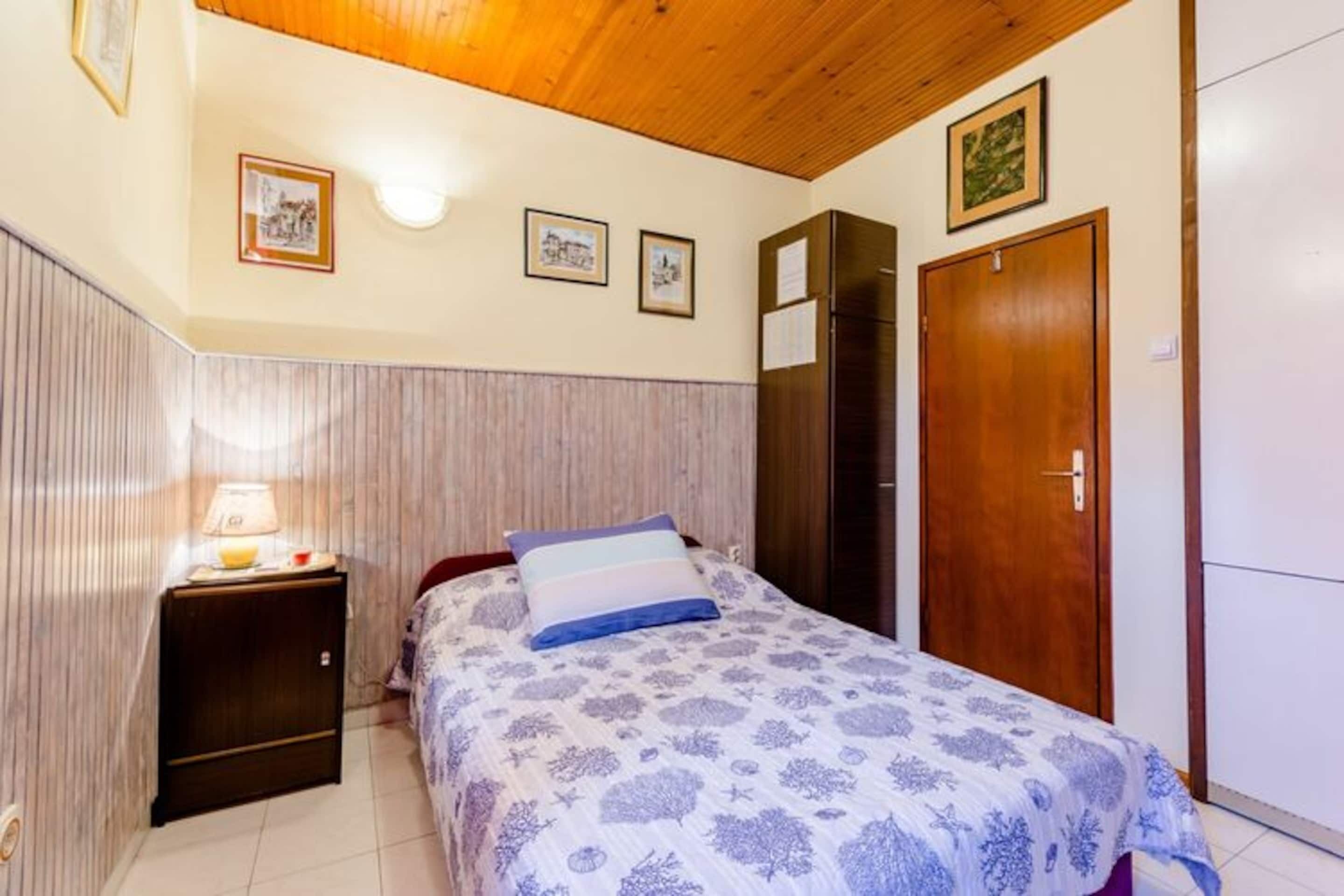 A bedroom with a bed, a nightstand, a wooden wardrobe, and a door.