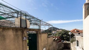 A narrow staircase leading to a building entrance with a metal gate, a street lamp, and a view of a town with red-roofed houses in the background. - Sunset Bay Room - Double Room With Terrace and Partial Sea View (Dubrovnik)