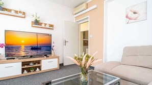 A modern living room with a flat-screen TV, a glass coffee table, a beige sofa, and decorative shelves. - Apartments Blazevic - Comfort Two Bedroom Apt With Hot Tub and Sea View (Zupa dubrovacka)
