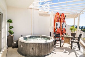 Ein Whirlpool auf einem Balkon mit zwei Stand-Up-Paddles, einem Tisch, Stühlen und Topfpflanzen.