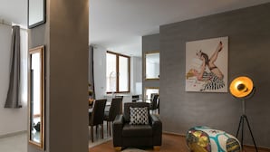 Een moderne woonkamer met een bank, een salontafel en een vloerlamp. In de achtergrond staat een eethoek met een tafel en stoelen.