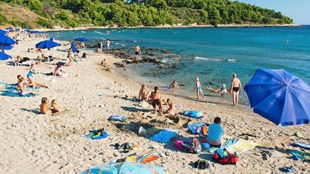 Ein Strand mit Menschen, die sonnenbaden und schwimmen, Sonnenschirmen und Handtüchern.