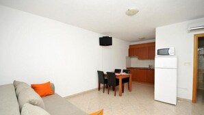 Ein Wohnzimmer mit einer Couch und einem Esstisch mit Stühlen. Es gibt eine Küchenzeile mit Schränken und einer Mikrowelle.