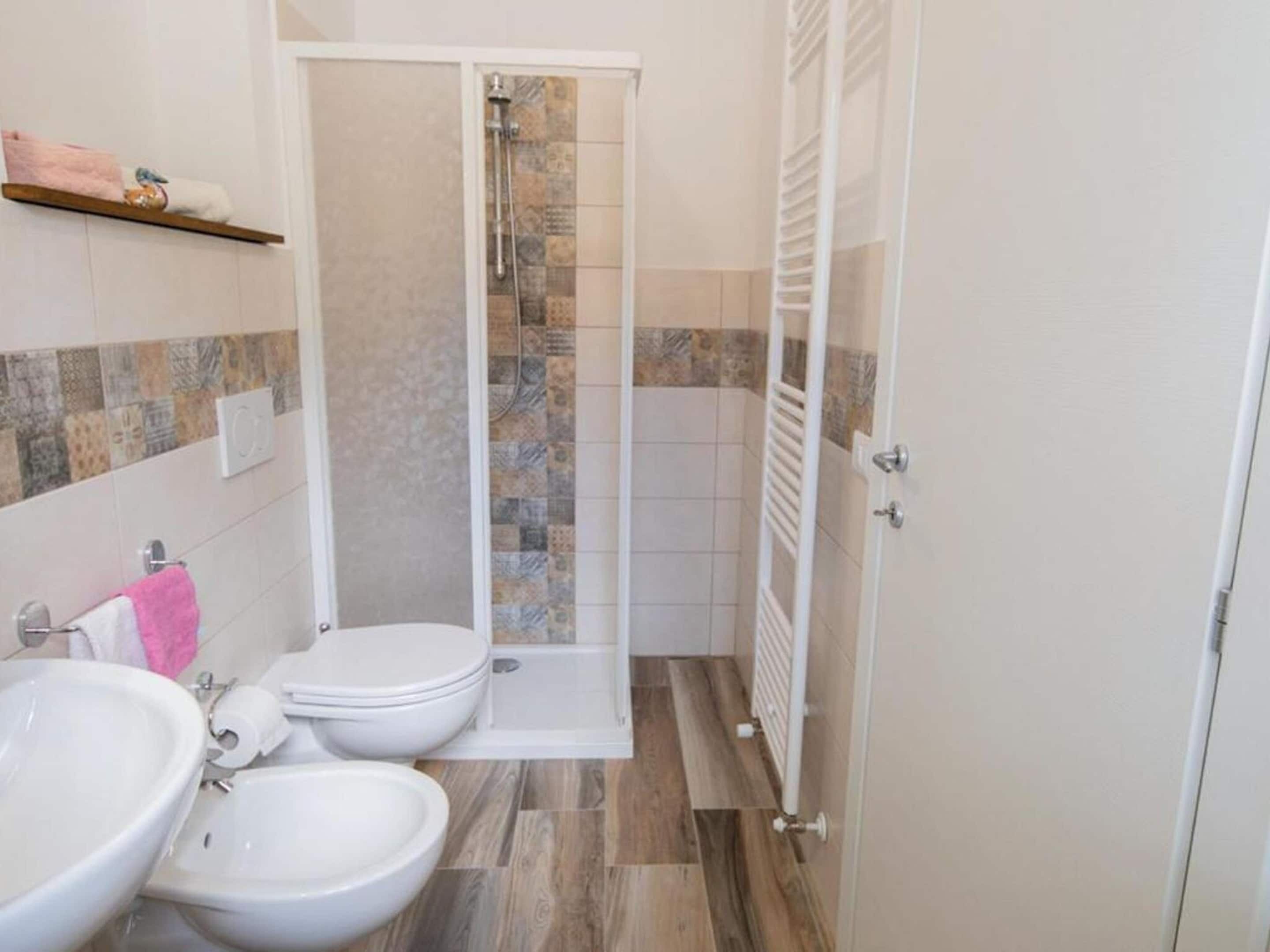 Un bagno con doccia, due servizi igienici, un lavandino e un portascopevoli.