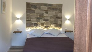 A bedroom with a stone wall headboard, two bedside lamps, a bed with a dark brown bedspread, and a hanging light fixture. - Villa in Montefalcone Appennino With Swimming Pool (Montefalcone Appennino)