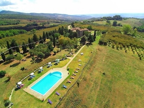 An aerial view of a property with a swimming pool surrounded by lounge chairs and umbrellas, set in a lush landscape with a stone building and a fence. - Belvilla by OYO Mansion in Orvieto (Orvieto)