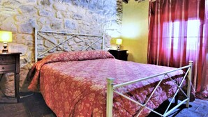 A bedroom with a stone wall, a metal bed frame, and a red bedspread. - Belvilla by OYO Mansion in Orvieto (Orvieto)