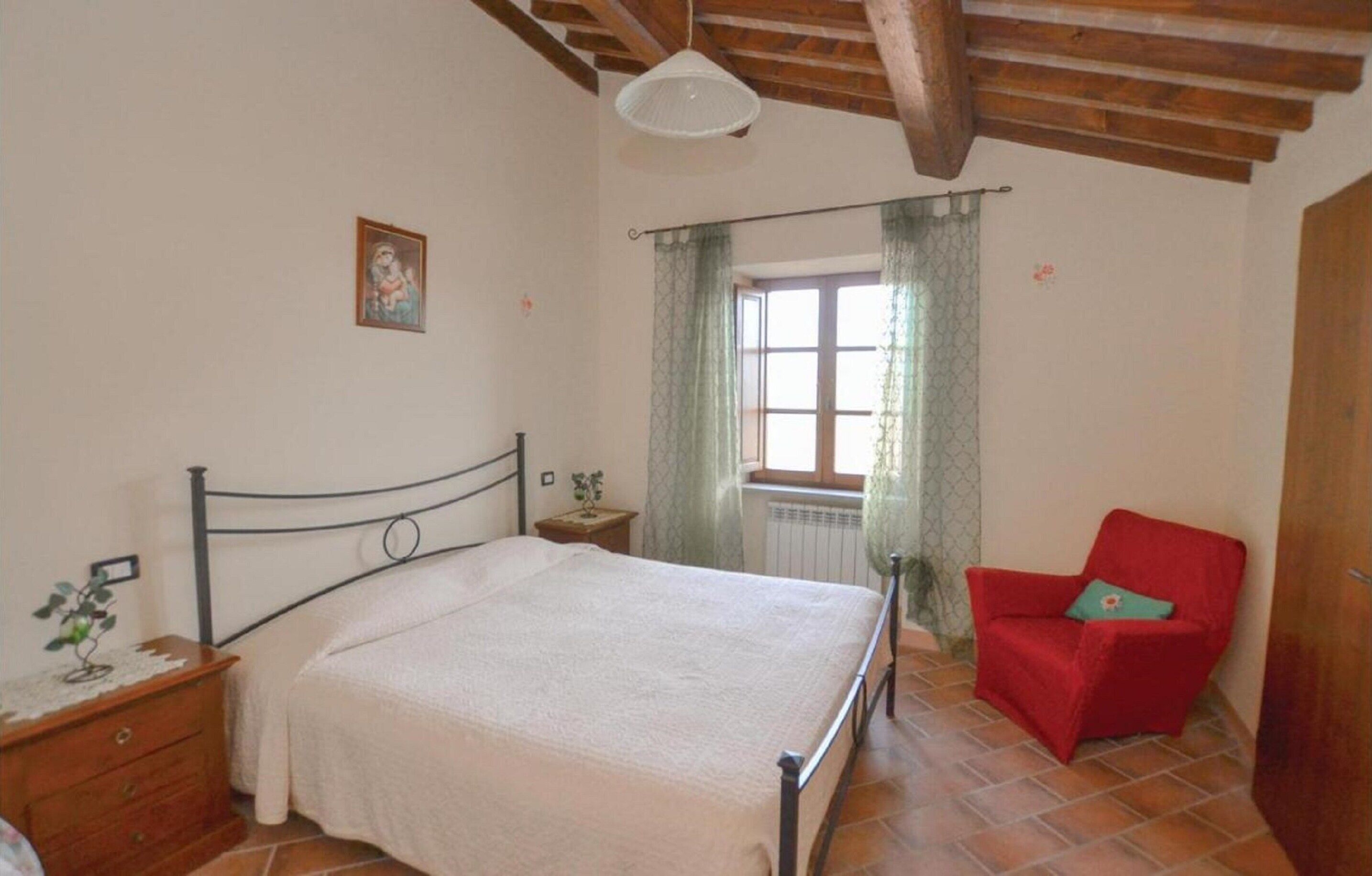 Una camera da letto con un letto, una sedia rossa, un comodino e una finestra con tende.