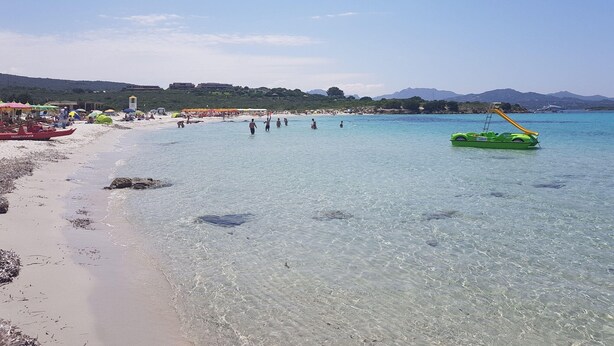 A beach with clear water, umbrellas, and a boat. - Apartment in Sardinia With Stunning Sea View (Olbia)