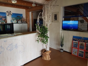 Un comptoir d’accueil en bois, une pancarte « Bienvenue à bord », un téléviseur diffusant des images de paysages et un tableau de menu fixé au mur.