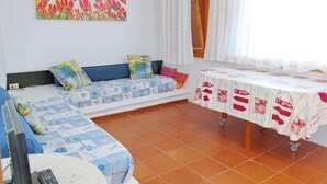 A room with a bed, a sofa, a table with a tablecloth, a painting on the wall, and a window with curtains. - Apartment in Sardinia With Stunning Sea View (Olbia)