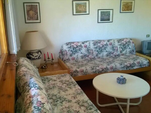 Uma sala de estar com sofás estampados em flor, uma pequena mesa com um objeto decorativo e quadros nas paredes.