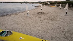 A beach with a yellow kayak, white umbrellas, and a calm sea. - Apartment in Olbia With Garden (Olbia)