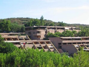 Un immeuble à plusieurs étages, doté d’un toit plat, entouré de verdure et de collines.