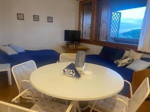 Um quarto com uma mesa redonda, cadeiras brancas, um sofá e uma televisão.