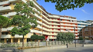 Un edificio residencial de varios pisos con balcones, entrada protegida por un portón y cielo despejado.