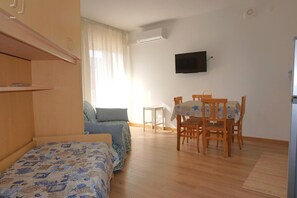 Un dormitorio con cama, una mesita, una silla, un televisor y una ventana con cortinas.