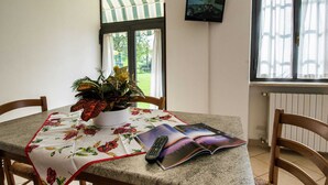 Zona de menjador amb una taula coberta per un mantell floral, una planta en test i una revista.