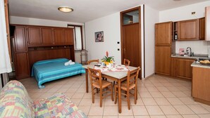 Un espai vital reduït amb llit, taula de dinar amb cadires, petita cuineta i un sofà.