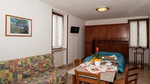 Una habitació acollidora amb un sofà estampat i de colors, una petita taula de menjador amb caires, un llit amb un llençol ratllat blau i blanc, armaris de fusta i un quadre encimbellat a la paret.