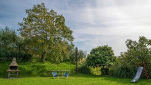 Un pati enjardinat amb una barbacoa, dues cadires blaves de jardí, un parc infantil i un tobogan.