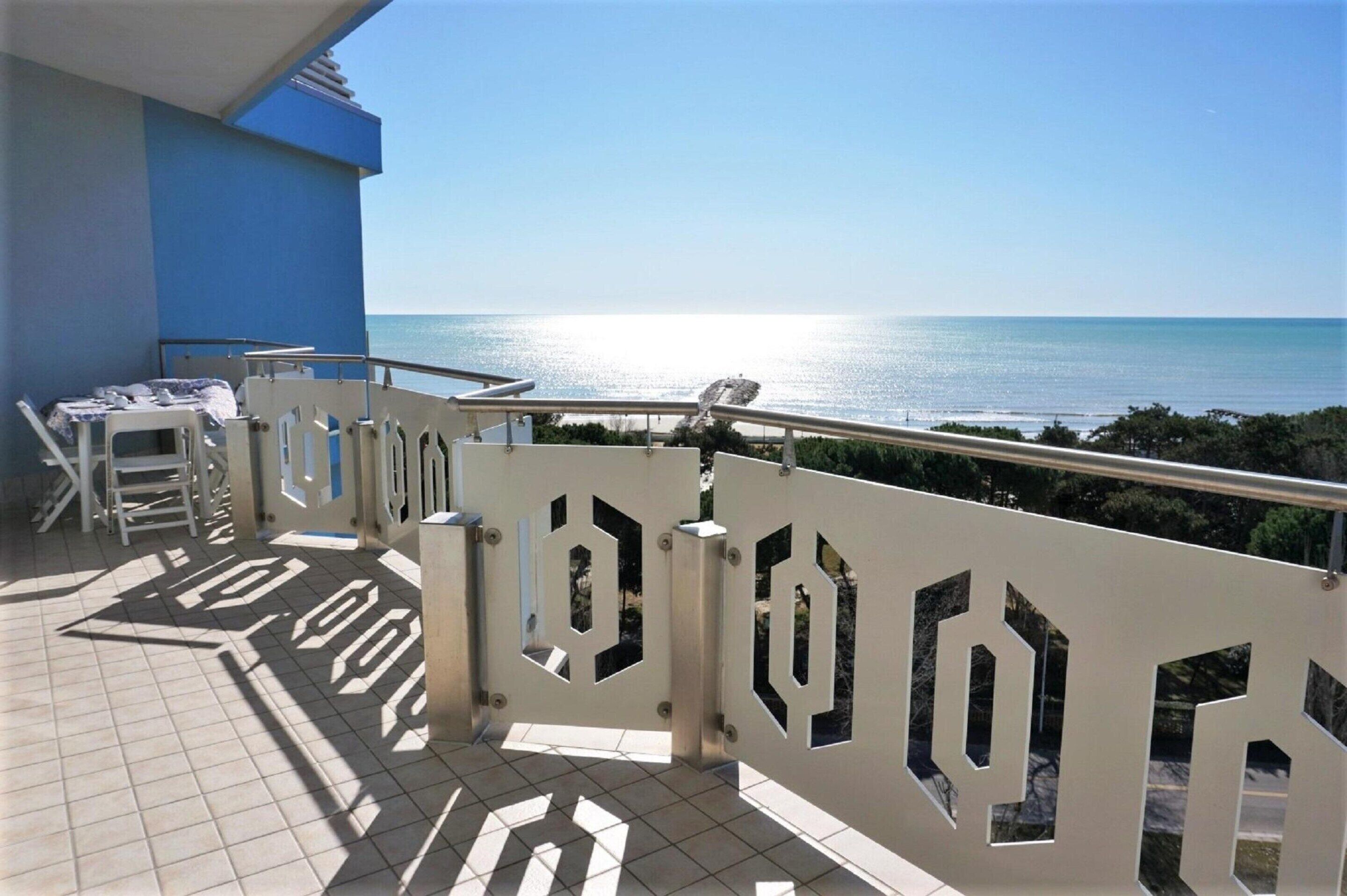 Ein Balkon mit Meerblick, ein Fliesenboden und ein weißes Geländer mit geometrischen Ausschnitten.