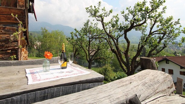 A wooden table with a bottle of champagne, a glass, and a flower on a mat, overlooking a mountainous landscape. - Belvilla by OYO Corno Nero (Ville di Fiemme)
