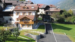 Un hôtel à la façade en pierre, doté de balcons en bois et d’une allée pavée menant à un espace de stationnement.