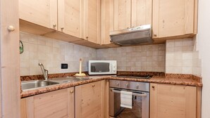 Une cuisine de taille réduite, dotée de meubles en bois, d’un évier en acier inoxydable, d’un four à micro-ondes et d’un four traditionnel.