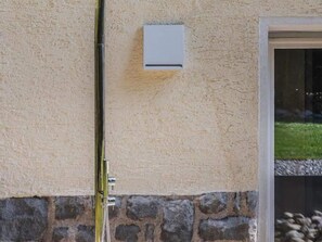 A building exterior with a stone base, a door with a glass panel, and a small white electrical box on the wall. - Belvilla by OYO Palm Loggia (Merano)