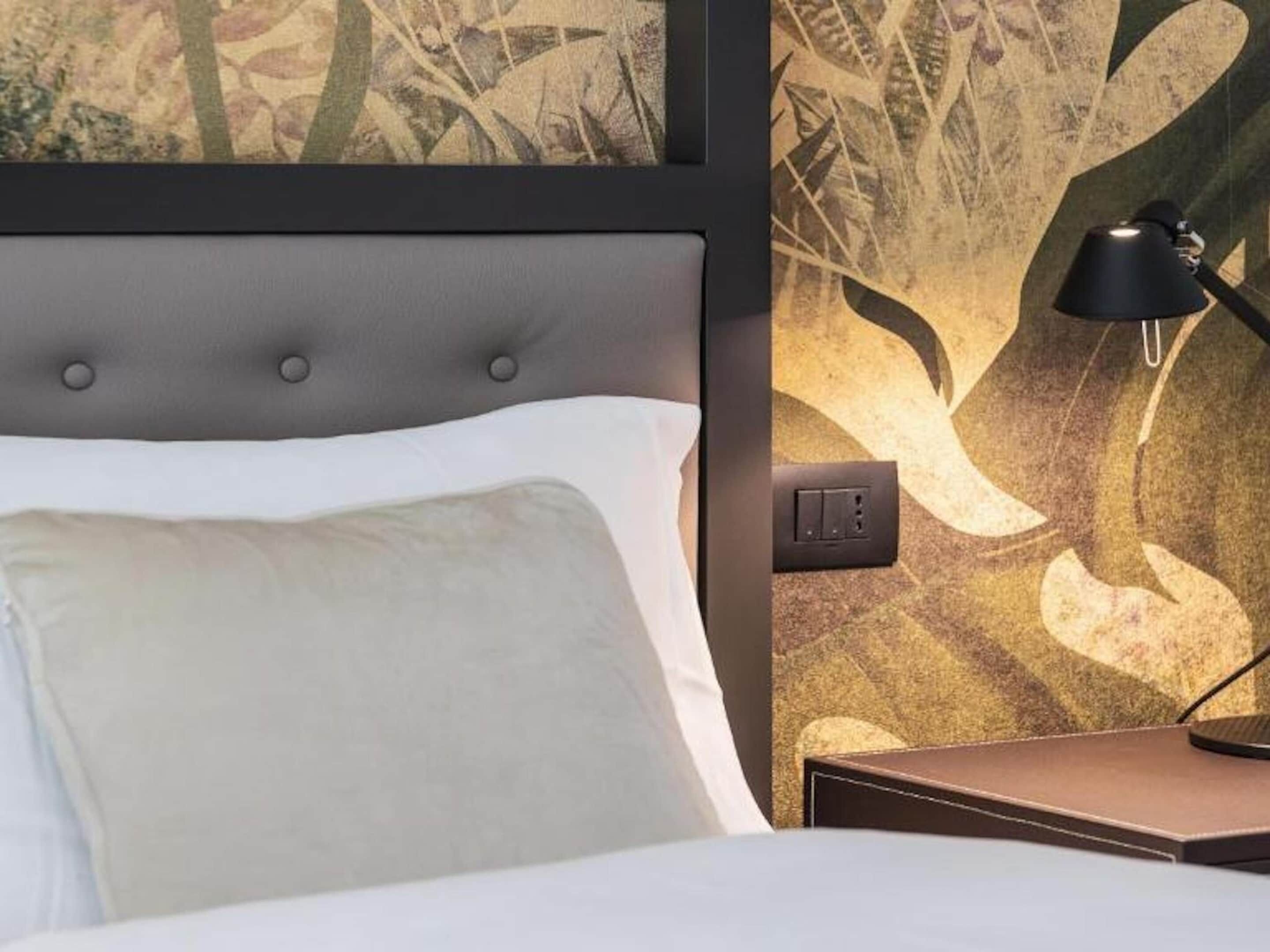A hotel room with a bed, a nightstand, a lamp, and a wall with a leaf pattern.
