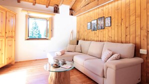 A cozy room with a wooden ceiling, a beige sofa, a glass coffee table, and a wooden cabinet. - Belvilla by OYO Casera Pantonio (Fonzaso)