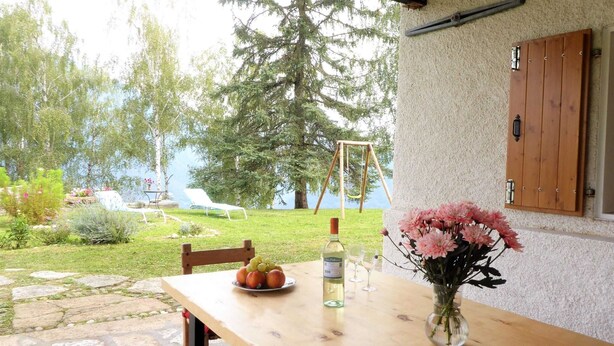 A wooden table with a bottle of wine, a plate of fruit, and a vase of flowers. - Belvilla by OYO Casera Pantonio (Fonzaso)