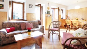 A cozy living room with a sofa, a wooden table, and a dining area with chairs and a table. - Belvilla by OYO Baita Silana (Pieve Tesino)
