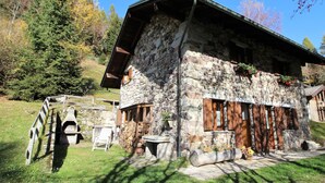 A rustic stone building with a sloped roof, wooden shutters, and a stone chimney. - Belvilla by OYO Baita Silana (Pieve Tesino)