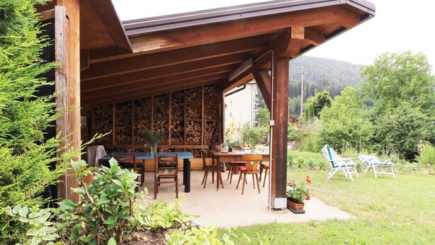 An outdoor dining area with wooden tables and chairs, surrounded by greenery and a mountain backdrop. - Family Retreat Near Garda (Ronzo-Chienis)