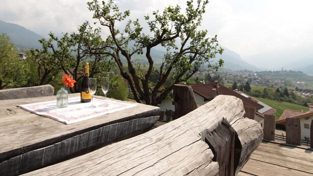 A wooden deck with a bottle of champagne and a glass on a table, overlooking a mountainous landscape. - Large Apartment With Terraces in Val di Fiemme (Ville di Fiemme)