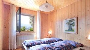 A wooden-paneled room with a bed, a window with curtains, a radiator, a wall-mounted lamp, and a framed picture. - Large Apartment With Terraces in Val di Fiemme (Ville di Fiemme)