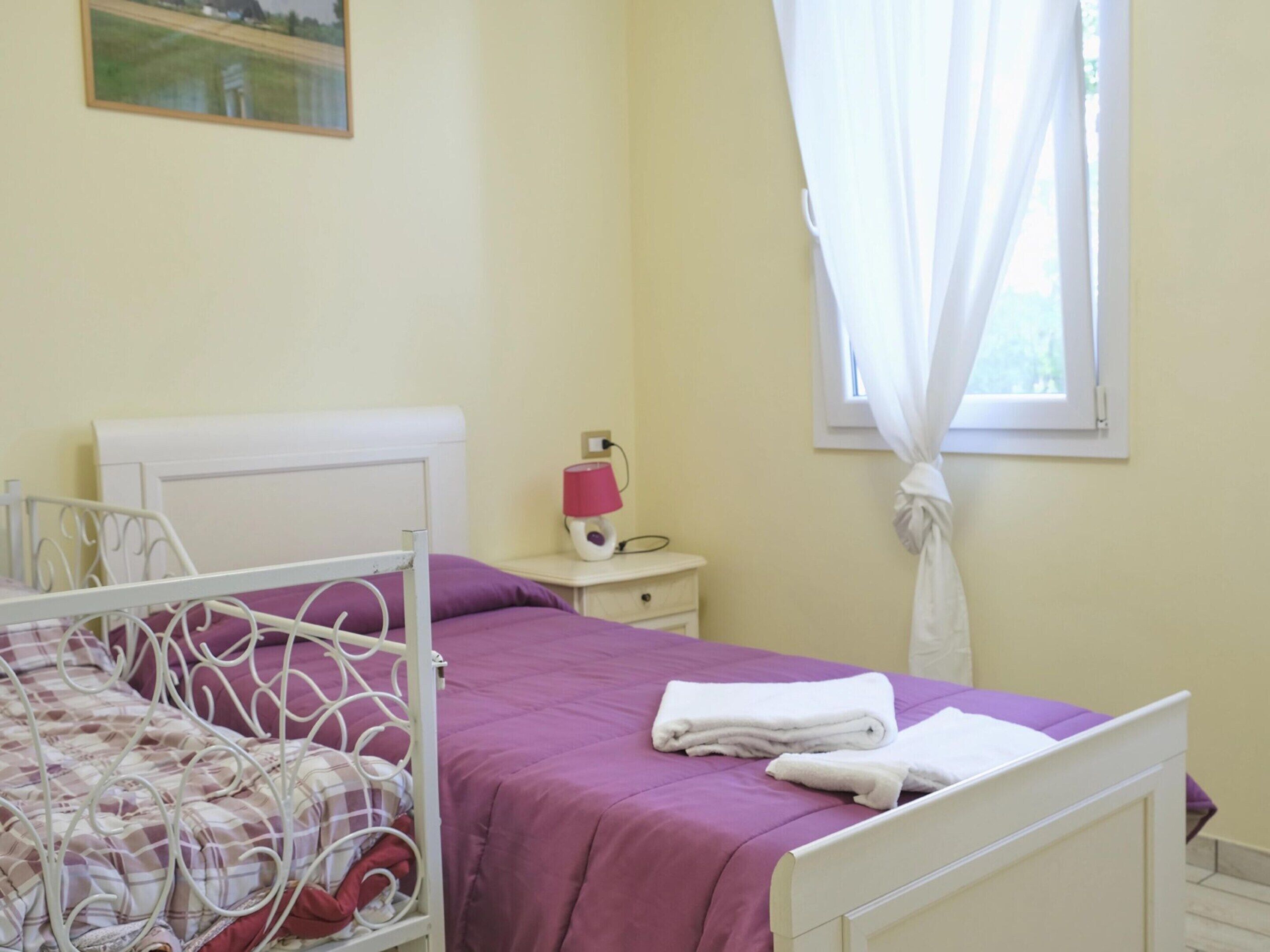 Un dormitorio con cama, mesita de noche, lámpara y ventana con cortinas.