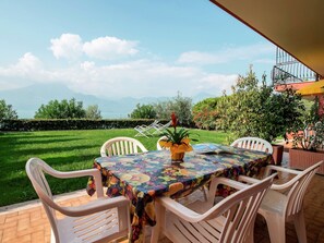 Eine Außenpatio mit Tisch und Stühlen, Blick auf einen Berg und See, und einem gepflegten Rasen.