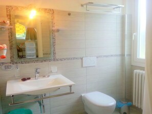 Ein Badezimmer mit weißem Waschbecken, Spiegel und Toilette. Ein Duschbereich mit Glastür und ein Handtuchhalter über dem Waschbecken.