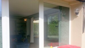 A room with a glass door leading to an outdoor area, a stone bench with a red cushion, and a bottle and glasses on the bench. - Belvilla by OYO Michael's House (Lesa)