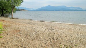 A pebbly lakeside with a single tree and distant mountains. - Belvilla by OYO Michael's House (Lesa)