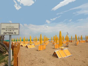 A beach with rows of yellow umbrellas and sun loungers, a sign indicating the beach is in concession, and the name 'ZATTERA 73'. - Holiday Home in Caorle Near Spiaggia Tartaruga (Caorle)