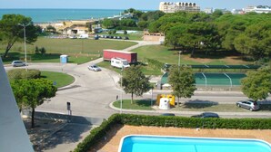 Blick auf eine Küstenregion mit Schwimmbad, einer Straße mit Autos und Gebäuden im Hintergrund.