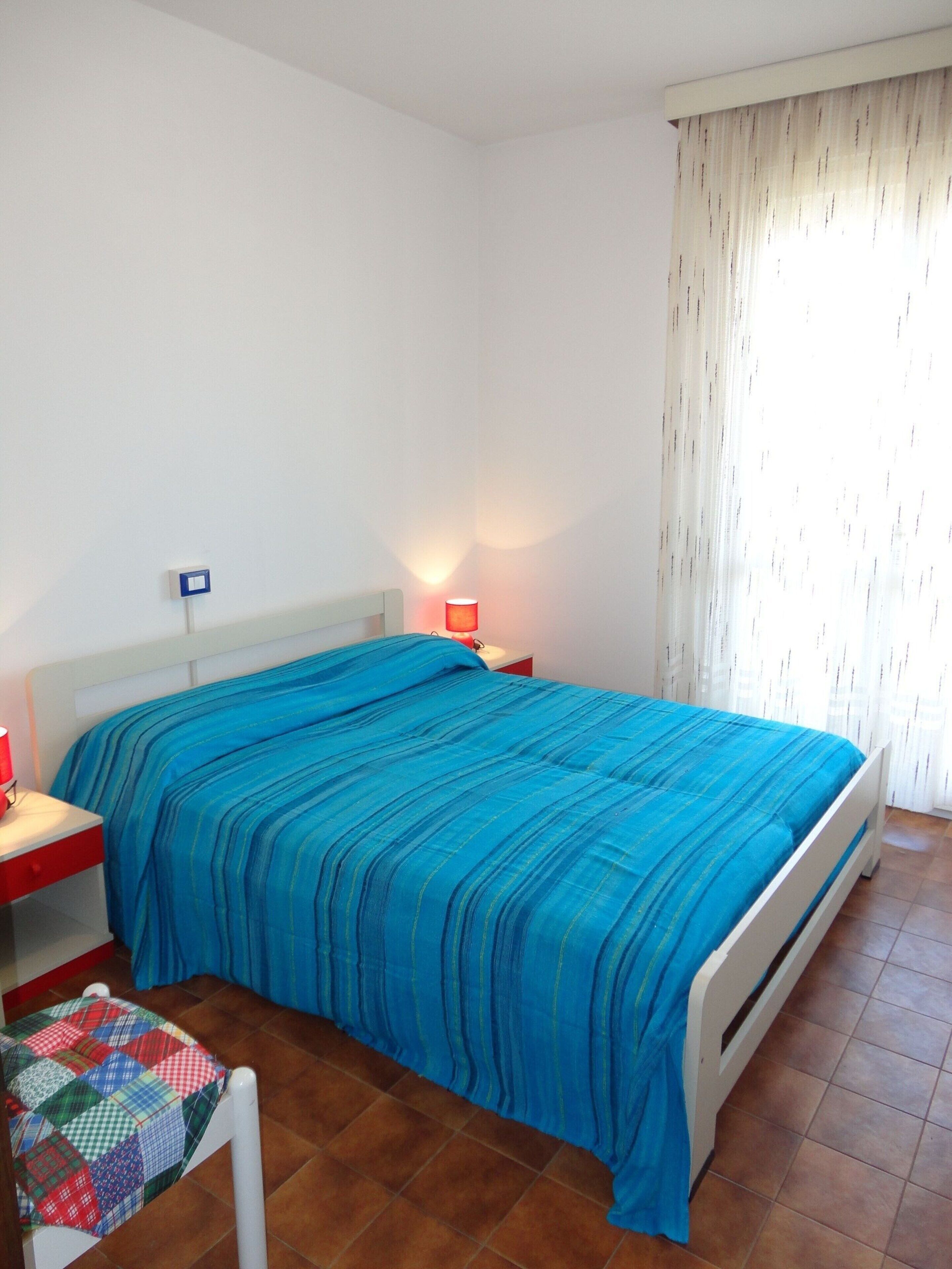 A bedroom with a bed, a nightstand, a lamp, and a window with curtains.