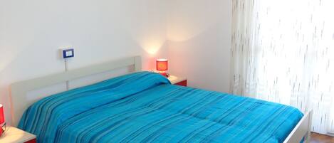 A bedroom with a bed, a nightstand, a lamp, and a window with curtains.