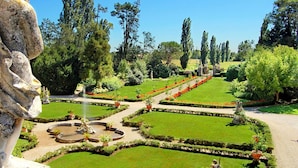 Ein formal gestalteter Garten mit einem zentralen Brunnen, gepflegten Rasenflächen und einer großen Steinstatue.